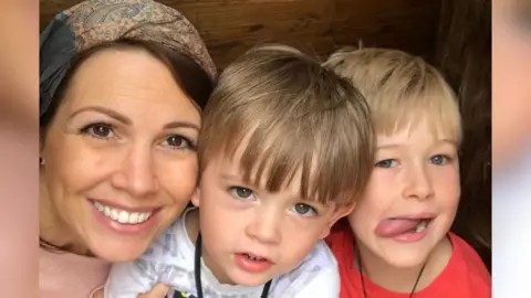 Natalie Hull Natalie Hull, wearing a pink top and smiling with her two sons one wearing a red t-shirt and the other wearing white.