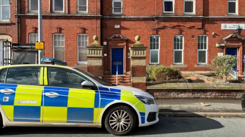 BBC A marked police car parked up outside a redbrick building in front of a blue door