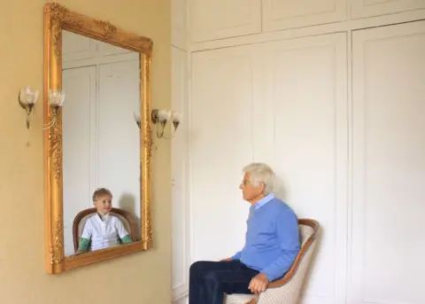 Antonia Wilford A man looks at a reflection of his younger self in the mirror
