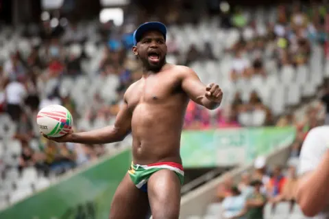 AFP A South African rugby supporter wearing flag-print swimming trunks throws the ball.