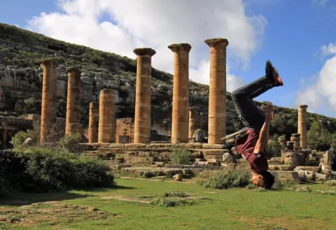 AFP A man jumps acrobatically next to a row of columns.