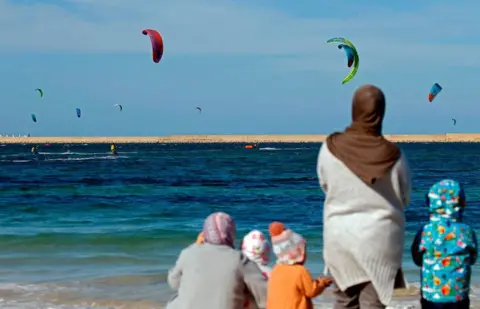 AFP Women and children watch a kite surfing tournament.
