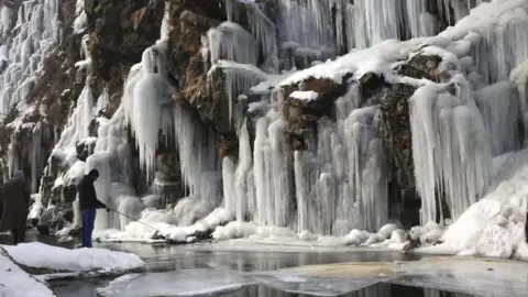 Farooq Khan / Shutterstock A man fishes near a frozen waterfall
