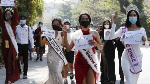 EPA Participants of beauty pageants flash the three-finger salute and hold placards as they march in front of the US Embassy during a protest against the military coup, in Yangon, Myanmar, 10 February 2021