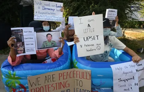 Getty Images Protesters hold up placards while sitting in plastic tubs during a demonstration against the February 1 military coup
