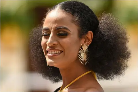AFP Esther Ajayi with her eyes closed. She is smiling and she has on gold earrings.