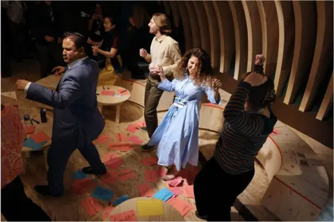 AFP People dancing with their arms in the air. The woman in the middle is smiling. There are pink and blue pieces of paper all over the floor.