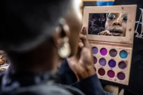 LUIS TATO/AFP A model gets her make up done before the main fashion show during the Kibera Fashion Week in the informal settlement of Kibera in Nairobi, on October 15, 2023. Kibera Fashion Week is a platform created from the community to redefine fashion and creativity while showcasing beauty and talent as a way to change the narrative about Nairobi's largest informal settlement.