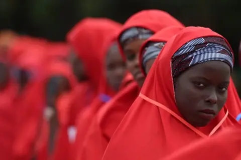 KOLA SULAIMON/AFP A bride dressed in red robe, looks on at the venue of a wedding reception at the Kano state governor's office after taking part in a mass wedding at the central mosque in Kano city, Kano State, Nigeria on October 14, 2023. The mass wedding is sponsored by the Kano State government in Nigeria to help widows and divorcees get remarried.