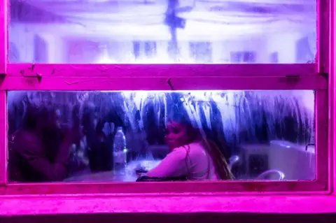 John Wessels/AFP A woman looks out of a dark bar that is surrounded in neon pink lighting, Dakar, Senegal - 21 January 2023