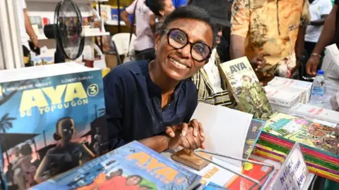 Issouf Sanogo/AFP Ivorian writer Marguerithe Abouet, author of comic book "Aya de Yopougon" poses for a photo during the Abidjan International Book fair in Abidjan on May 13, 2023.