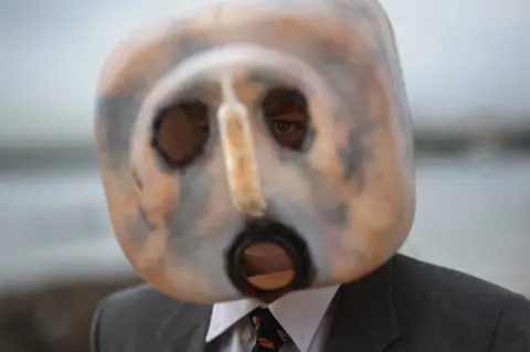 Rodger Bosch/AFP Man with a plastic mask on and a dark suit - 5 June 2023
