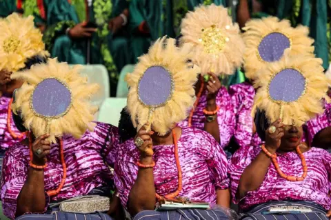 Samuel Alabi/AFP Women cover their faces with stitched, feathered fans in Ijebu, Ogun state, Nigeria - 30 June 2023