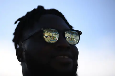 Matthias Hangst/Getty Images Talla Diop stands in the shade with bright reflections on his sunglasses, Paris, France - July 2023