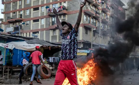 Luis Tato/AFP An opposition supporter chants slogans as he faces Kenya police officers during clashes at the informal settlement of Mathare in Nairobi, Kenya - 27 March 2023