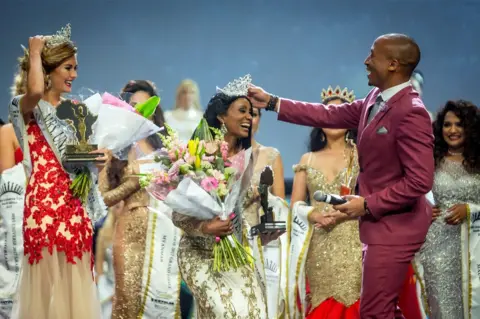 AFP Mrs. Gabon Gwen Madiba reacts after her crown fell on the floor and is re- placed by television host and personality Arthur Evans (R) during the Mrs. Universe beauty pageant on September 02, 2017, at the International Convention Centre in Durban. Mrs. Universe must age 25 to 45, have a family, her own career, and be involved with a significant cause in favour of other people.