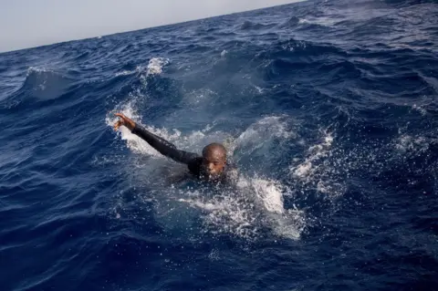 AFP A migrant tries to board a boat of the German NGO Sea-Watch in the Mediterranean Sea on November 29, 2017. During a shipwreck, five people died, including a newborn child. According to the German NGO Sea-Watch, which has saved 58 migrants, the violent behavior of the Libyan coast guard caused the death of five persons.