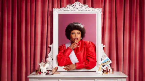 Shakespeare's Globe Anne Odeke wearing a crown and a red dress. 
She is standing by a vanity table and has emerged herself in the mirror and has her index finger on her lips.