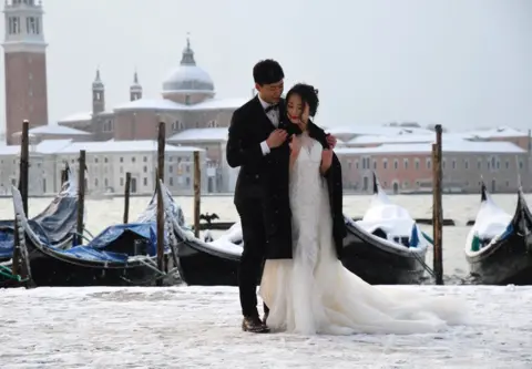 ANDREA PATTARO/ AFP A couple poses in St. Mark's Square in Venice following an overnight snowfall.