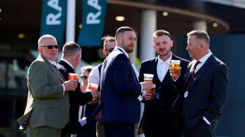 PA Media A group of six men wearing suits and drinking pints at Aintree.