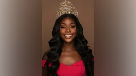 Martin Higgs A woman with long black hair smiles while wearing a golden crown and a red dress.
