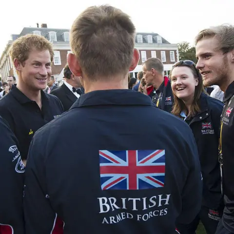 Geoff Pugh - WPA Pool/Getty Images The back of man's jacket is emblazoned with a Union Jack flag and the words: British Armed Forces. He is stood in front of Prince Harry in a crowd of people