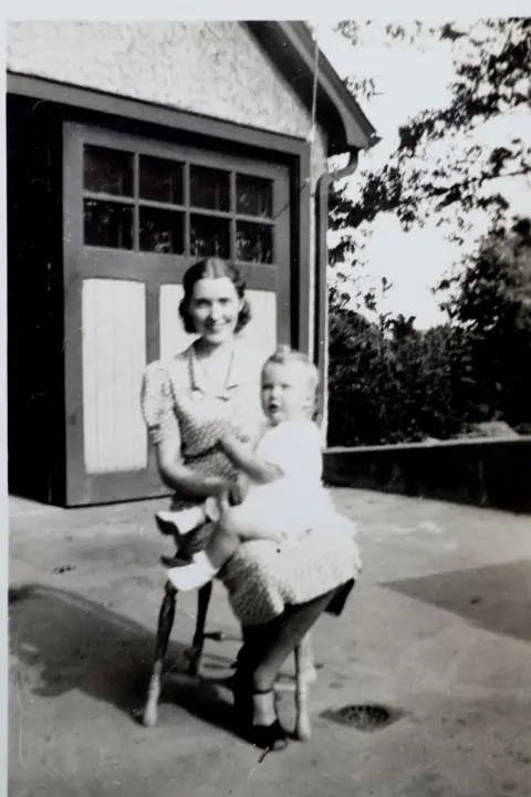 Getty Images Trump's mother, Mary Anne MacLeod, is facing the camera as she sits with baby Maryanne, Donald's sister, in her lap. They are outside in front of double doors and it's 1938