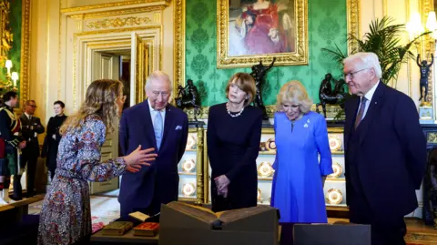 Reuters The King and Queen stand in an ornate, green-walled room beside the German president and his wife. They are stood in a row in front of a low table on which old books are positioned.
